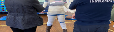 Person wrapped in bandages with instructors assisting in a training session.