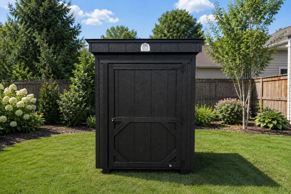 Black wooden shed in a green backyard under a blue sky.