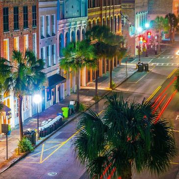Night scene of a city street with palm trees and historic buildings.
