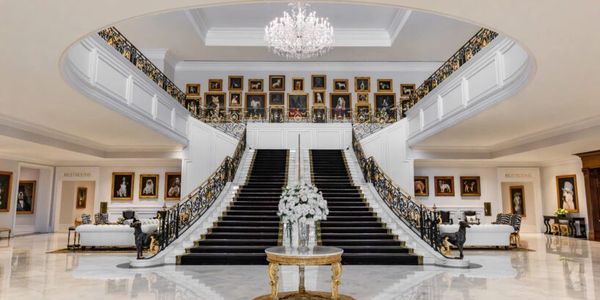 Grand staircase in a luxurious mansion with portraits and chandelier.