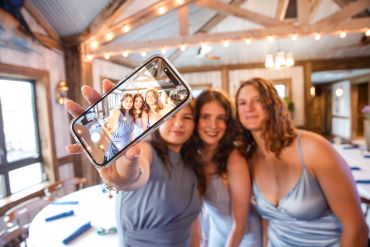 Three women in blue dresses taking a selfie at a decorated venue.
