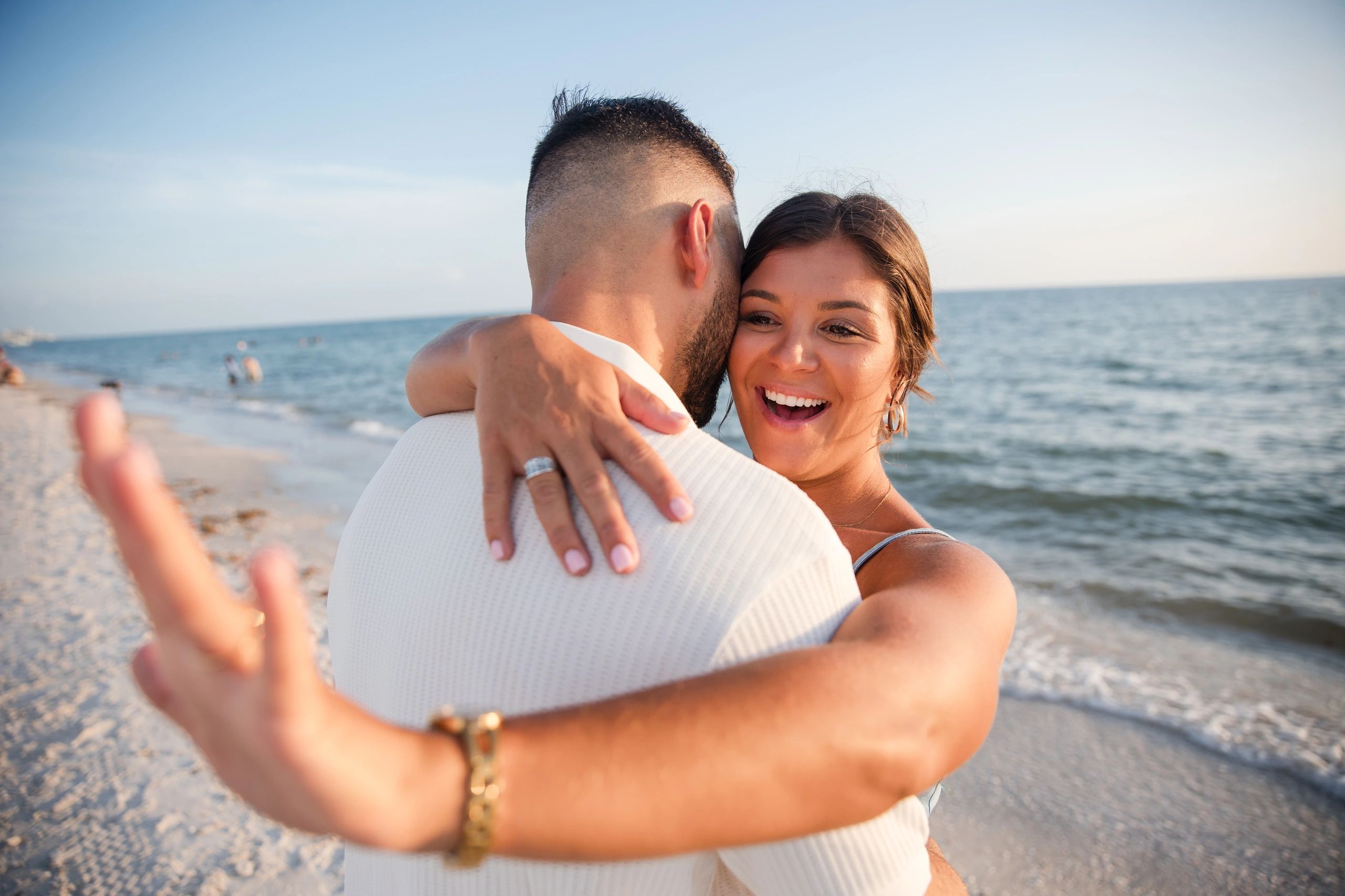 A bride smiling as she embraces her groom beside the ocean.