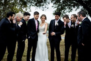 Bride and groomsmen in suits sharing a joyful moment outdoors.