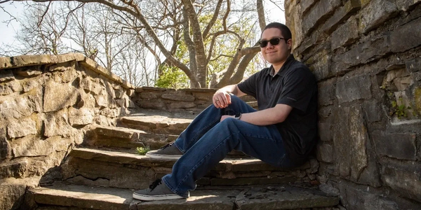 Man wearing sunglasses sitting on stone steps outdoors on a sunny day.