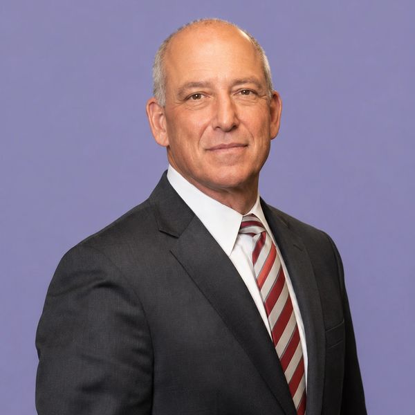 Confident middle-aged man in a suit against a purple background.