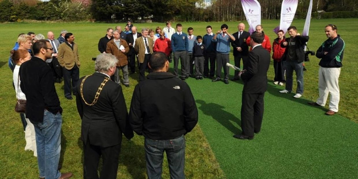 Group gathers outdoors for an event on a grassy field with banners.