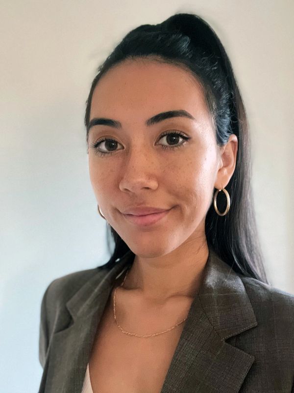 Young woman with hoop earrings and a blazer smiling.