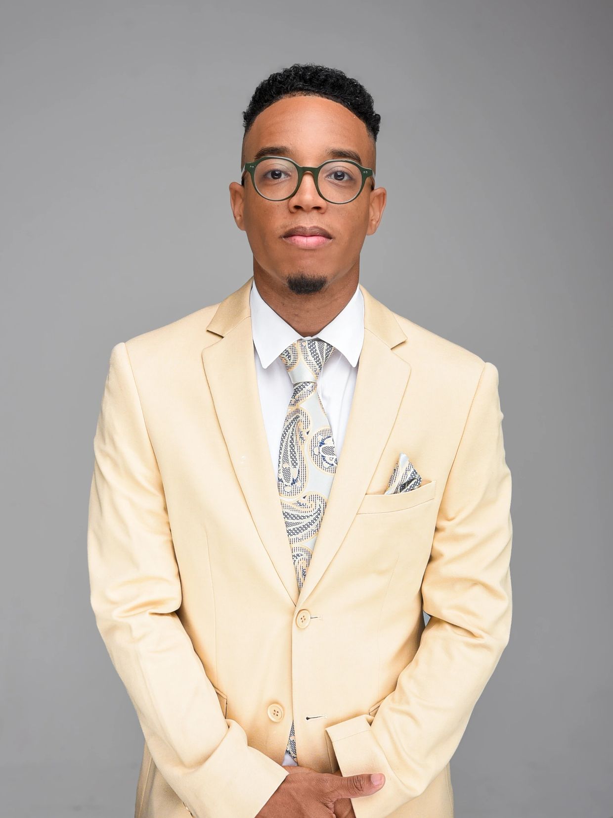 Man in beige suit and glasses posing.