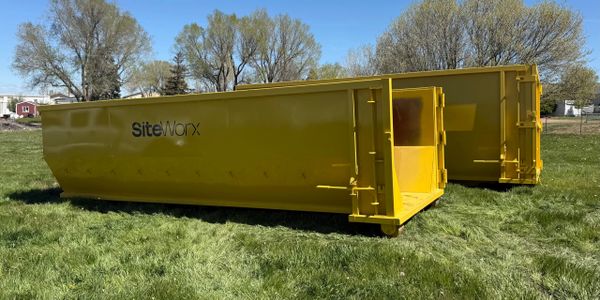 Two large yellow dumpsters labeled 'SiteWorx' on a grassy field under a clear sky.