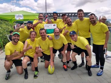 A cheerful rugby team in yellow jerseys posing with a trophy outdoors.