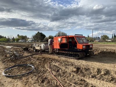 Orange tracked vehicle on muddy field with a person nearby.