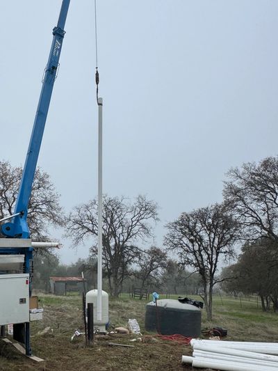 Crane lifting a long white pipe outdoors.