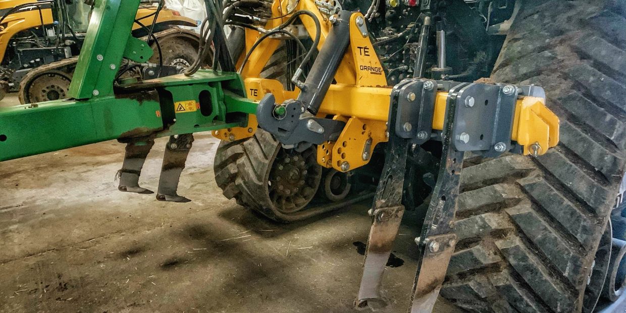 Close-up of tractor attachments with sharp metal tines and large tires in a barn.