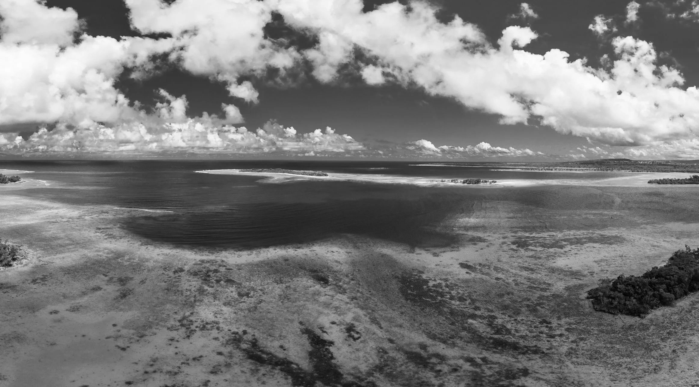 Aerial view of tropical islands surrounded by clear turquoise waters and a blue sky with scattered clouds.