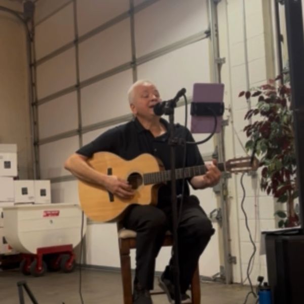 Man singing and playing guitar in an indoor setting.