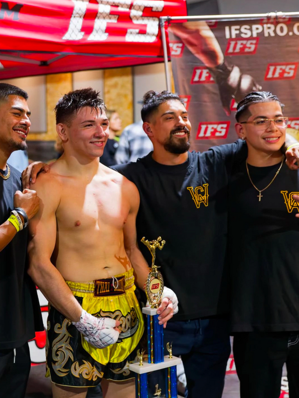 A victorious Muay Thai fighter with his team holding a trophy.