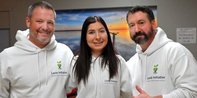 Three people smiling, wearing white hoodies with Levie Initiative logos.