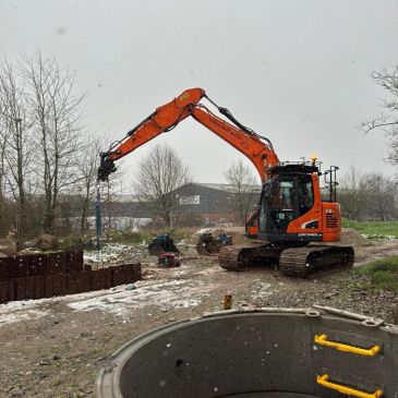 Orange excavator operating outdoors in snowy conditions.