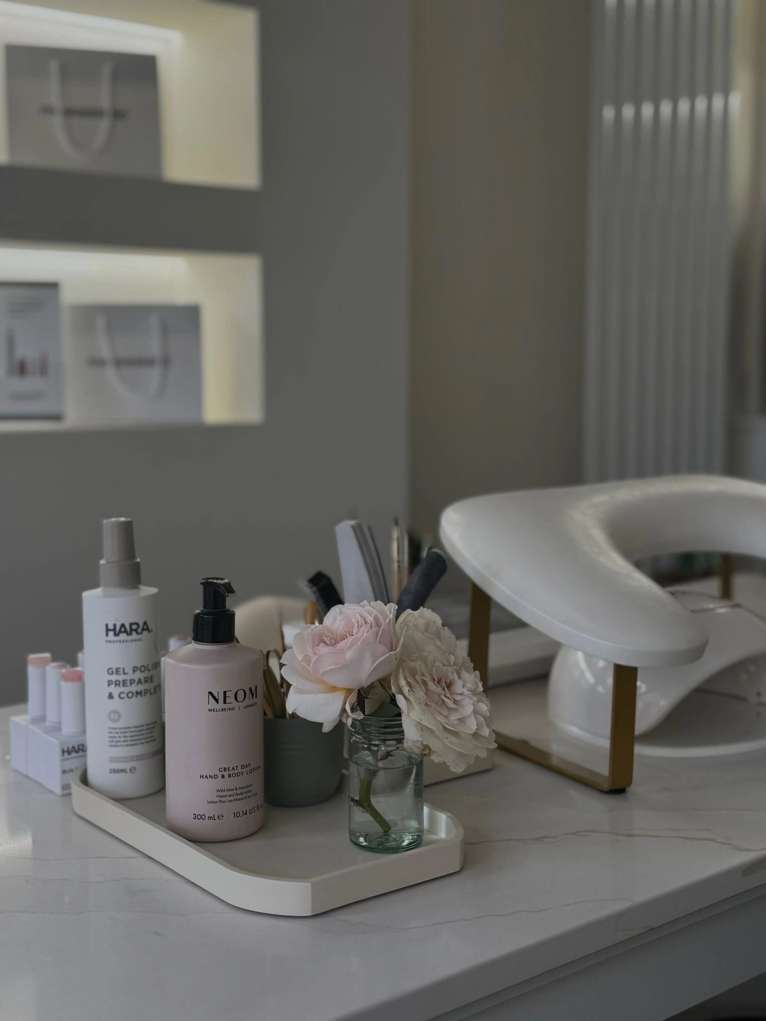 A tray with skincare products and flowers on a marble table in a cozy room.