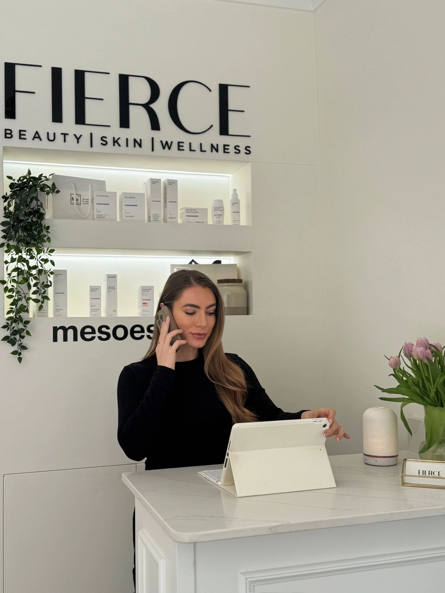 A woman working at a beauty and wellness reception desk, talking on the phone.