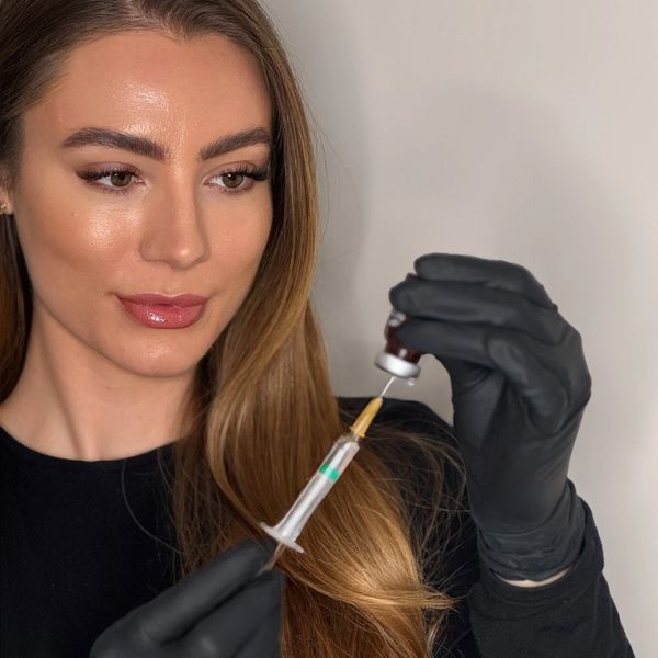 A woman in black gloves draws liquid into a syringe from a vial.