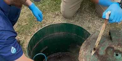 Two people with blue gloves inspecting a green underground tank or well.