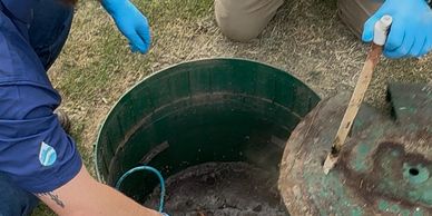 Two people with blue gloves inspecting a green underground tank or well.