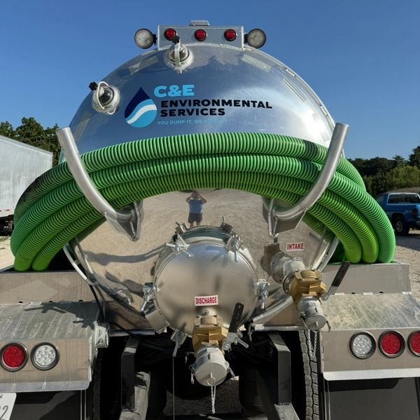 The back of a silver tank truck from C&E Environmental Services, featuring green hoses and labeled i