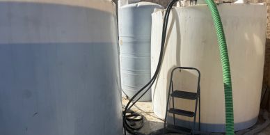 Large white storage tanks with hoses and a ladder in an industrial setting.