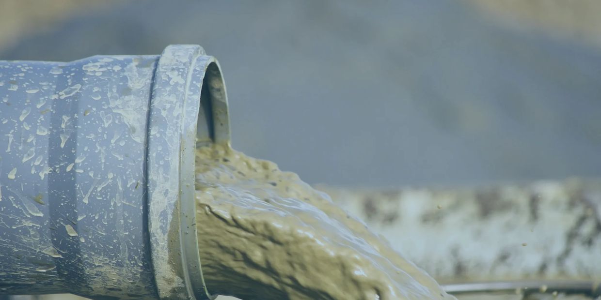 A gray pipe spills thick, brown sludge, showcasing a messy and industrial environment.