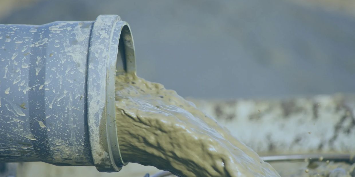 A gray pipe spills thick, brown sludge, showcasing a messy and industrial environment.