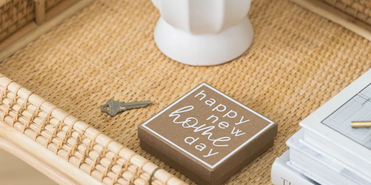 House key and "Happy New Home Day" gift box on a rattan tray with closing documents - Delia Hines bu