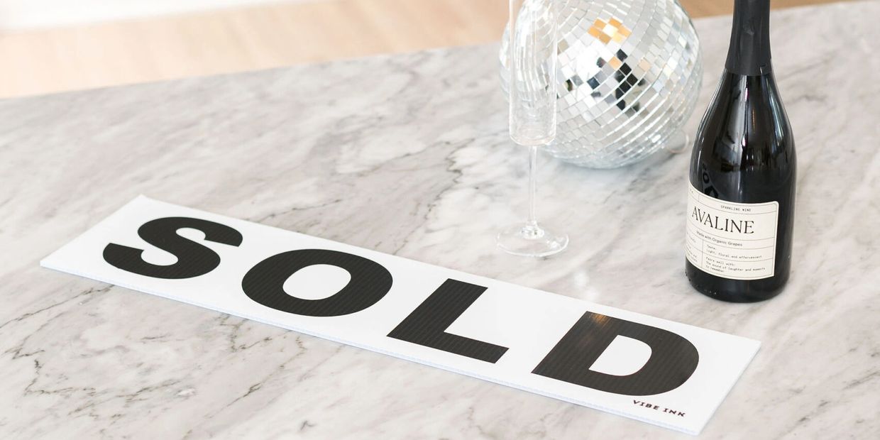 SOLD sign on marble countertop with champagne bottle and disco ball celebrating a successful home sa