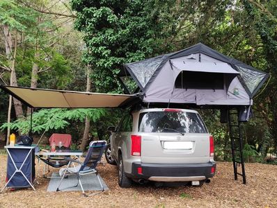 Car with rooftop tent and camping setup in a forest.