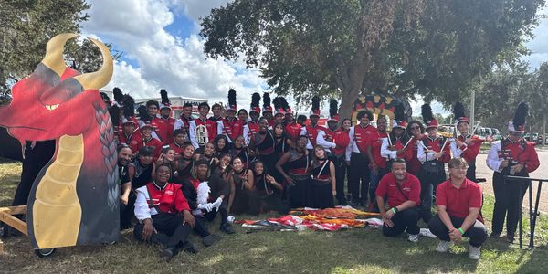 High school marching band posing outdoors in uniform with a dragon prop.
