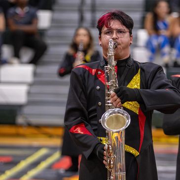 A saxophonist in a black and red uniform plays in a gymnasium.