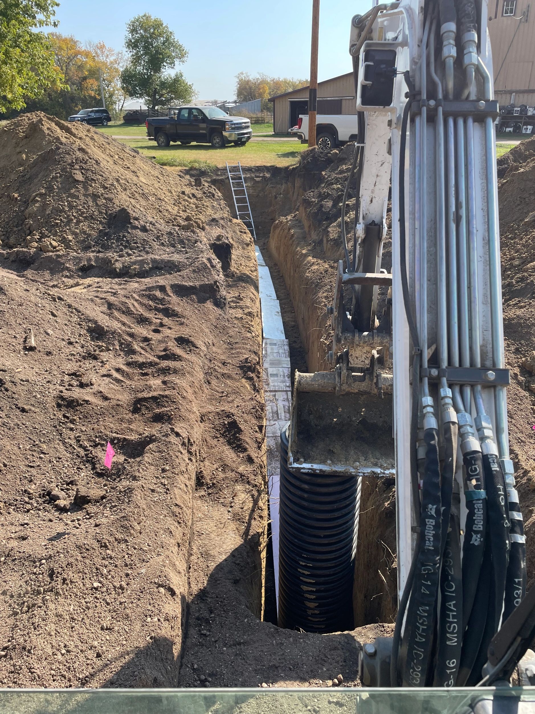 Excavator installing a large drainage pipe in a deep trench at a construction site.