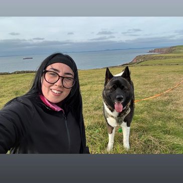 Woman and dog selfie on grassy hill by the sea.