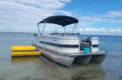 A pontoon boat anchored in shallow water under a blue sky.