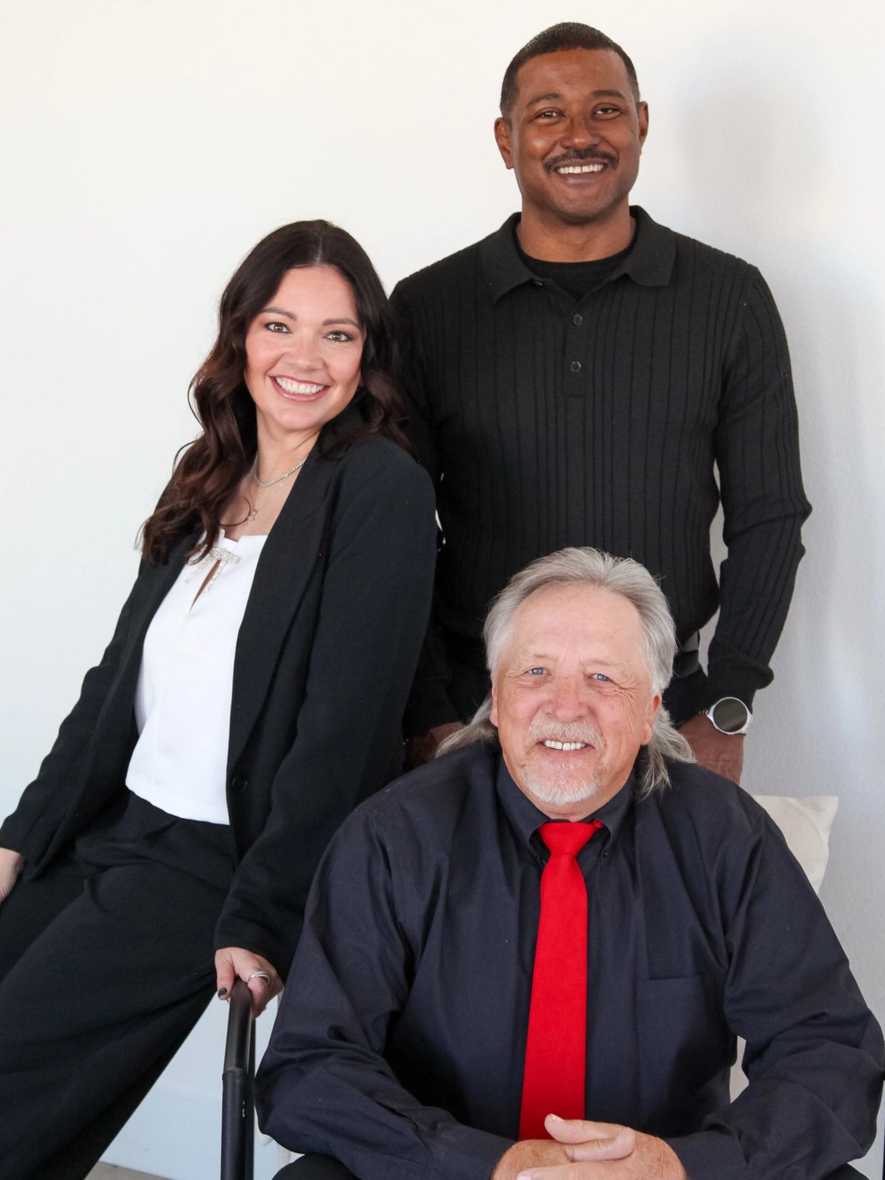 Three professionals smiling, dressed in black, with a man in a red tie sitting in front.