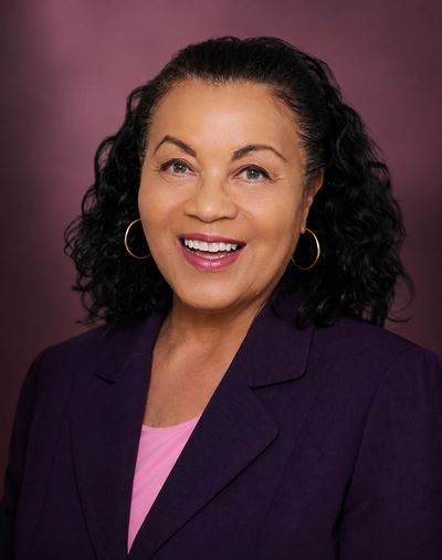 Smiling woman with curly hair in purple blazer.