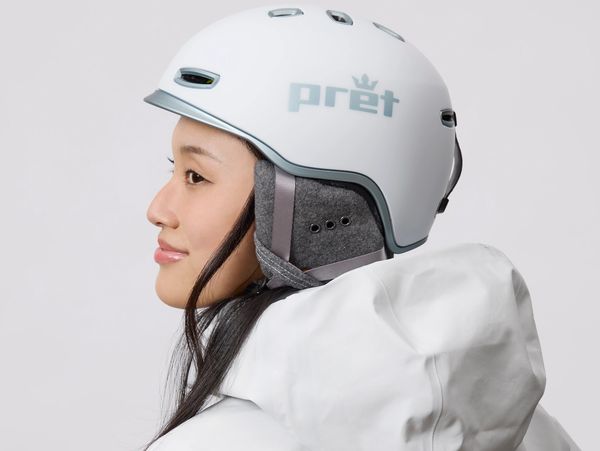 Woman wearing a white Pret helmet and white jacket against a plain background.
