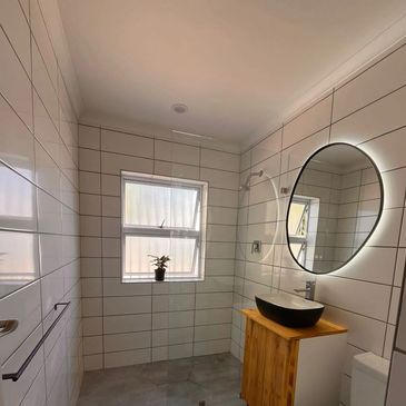 Modern bathroom with white tiles and a wooden vanity under a round mirror.