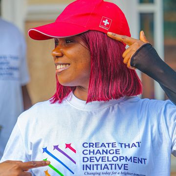 Woman in red cap pointing at her head, wearing a motivational T-shirt.