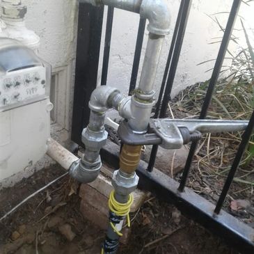 A wrench tightening a pipe fitting on an outdoor gas line setup.