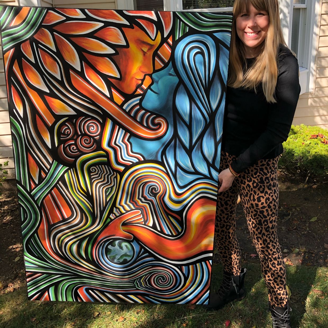 Leah Wake standing with a canvas print of her painting Sowing Seeds of Light in 2020.