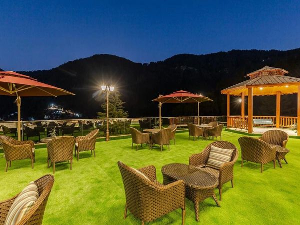 Outdoor seating area with wicker furniture and umbrellas on green turf at dusk.