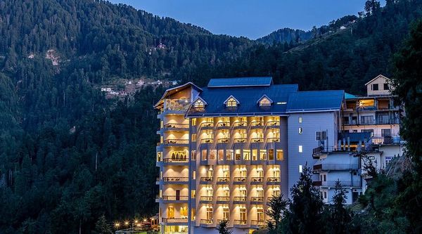 Illuminated hotel nestled in a forested mountain landscape at dusk.