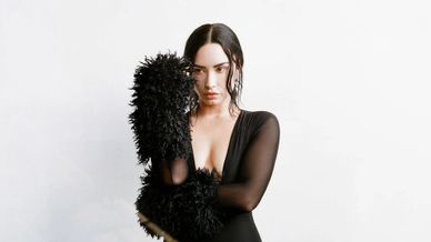 Woman in black dress with feathery gloves posing against white background.