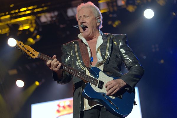 Elderly man passionately playing electric guitar on stage with microphone headset.